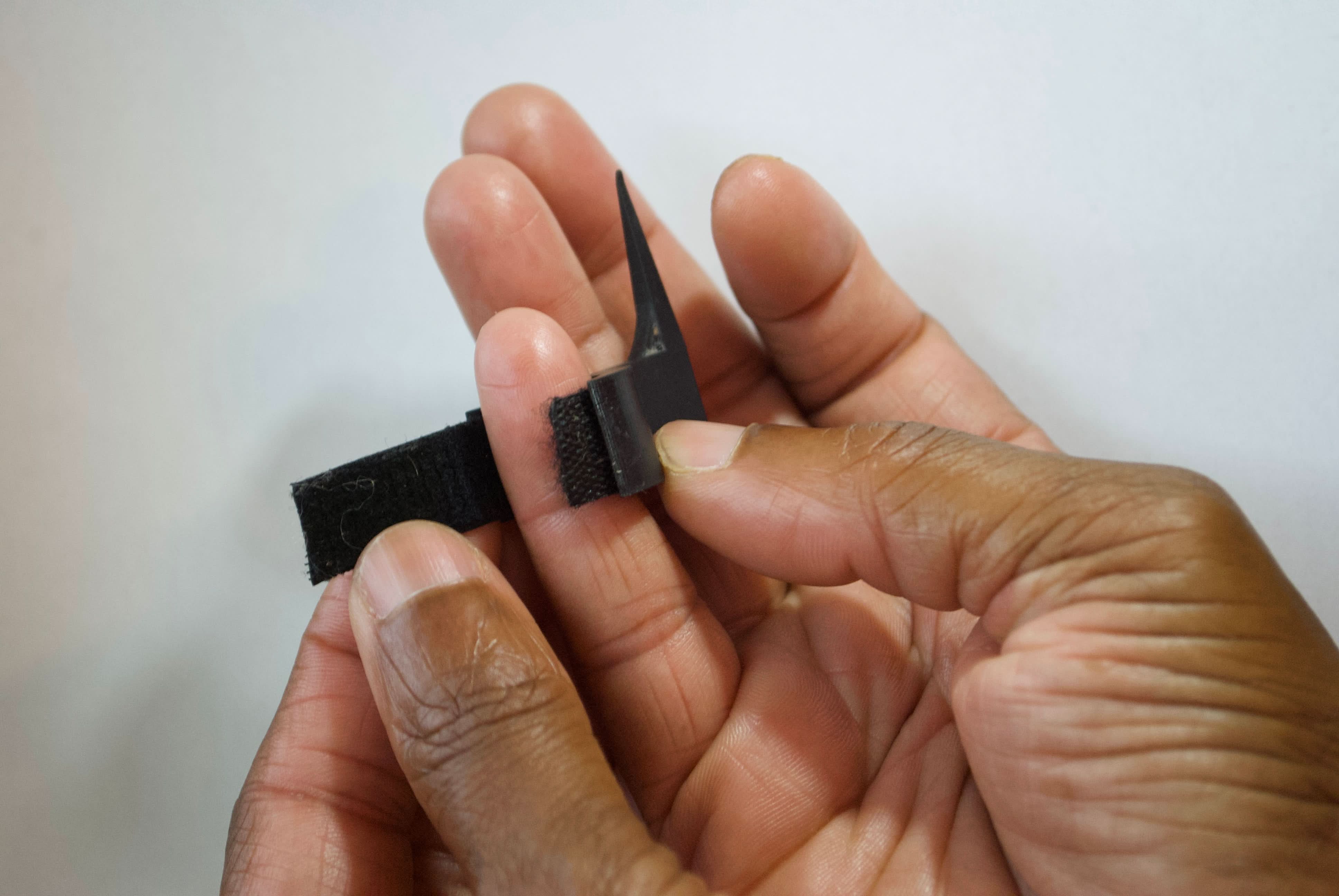 Close-up of hands adjusting The Braid Aid- Adjustable Finger Parting Tool with Velcro strap for secure fit during braiding.