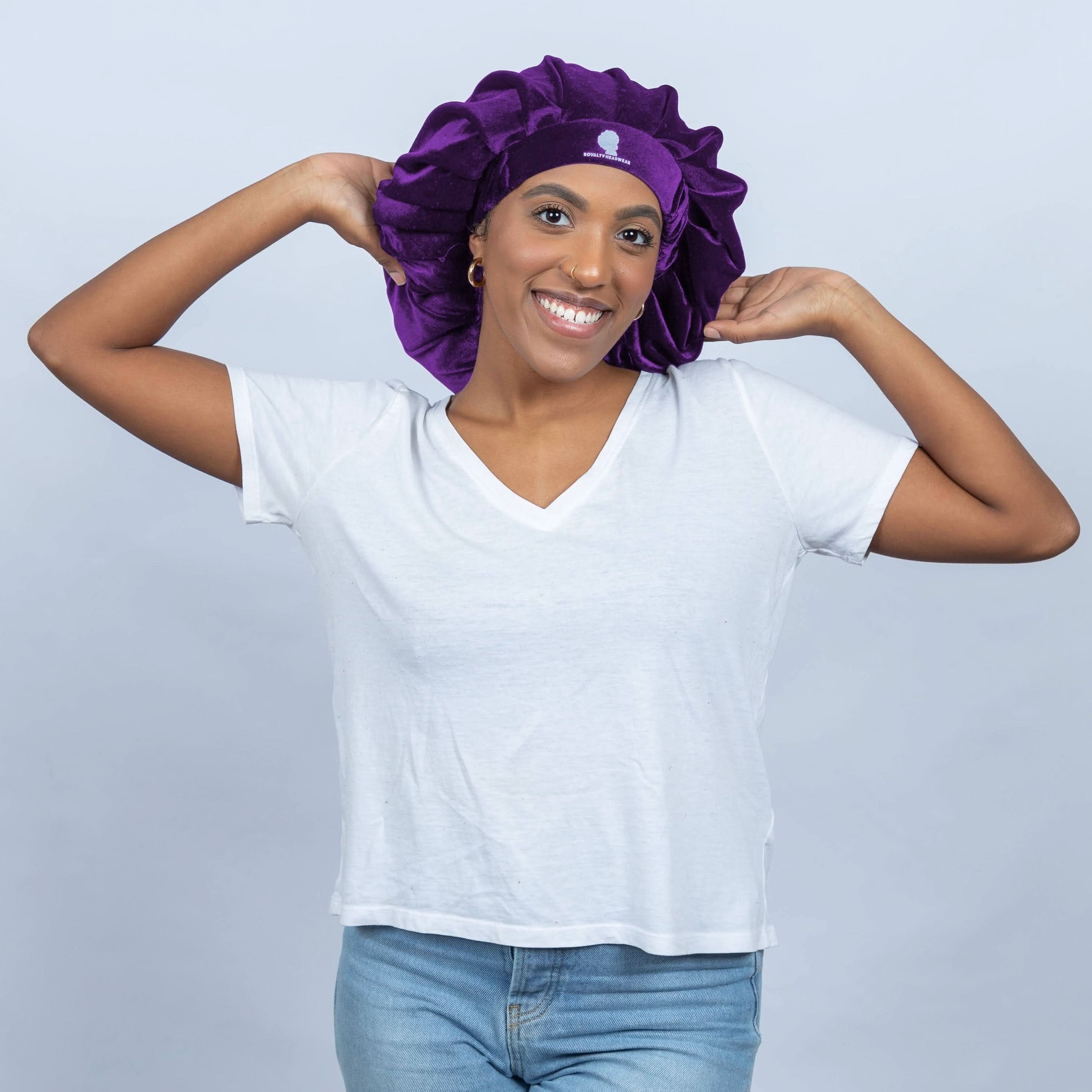 The Royalty Bonnet in purple velvet, a jumbo silk bonnet for hair care and nighttime use, shown on a smiling model in a white shirt.